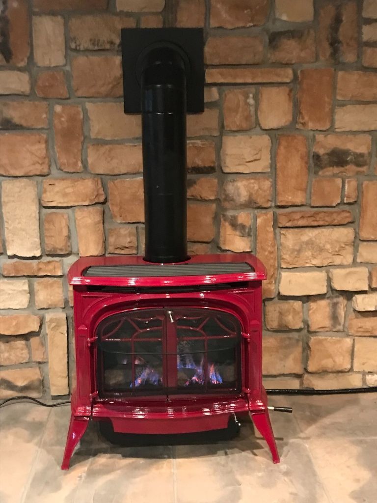 A red wood stove is sitting in front of a stone wall.