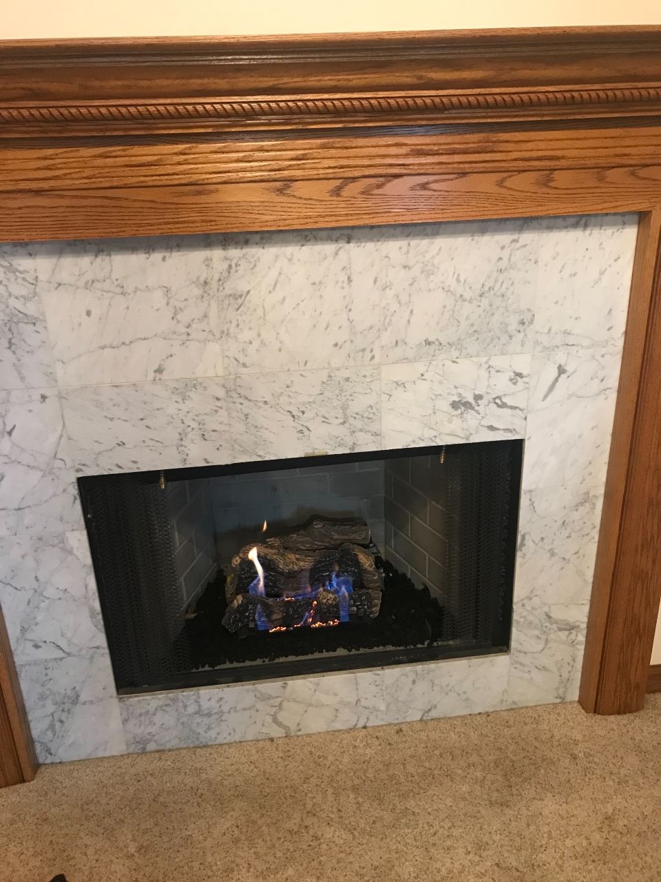 A fireplace with a marble surround and a wooden mantle in a living room.