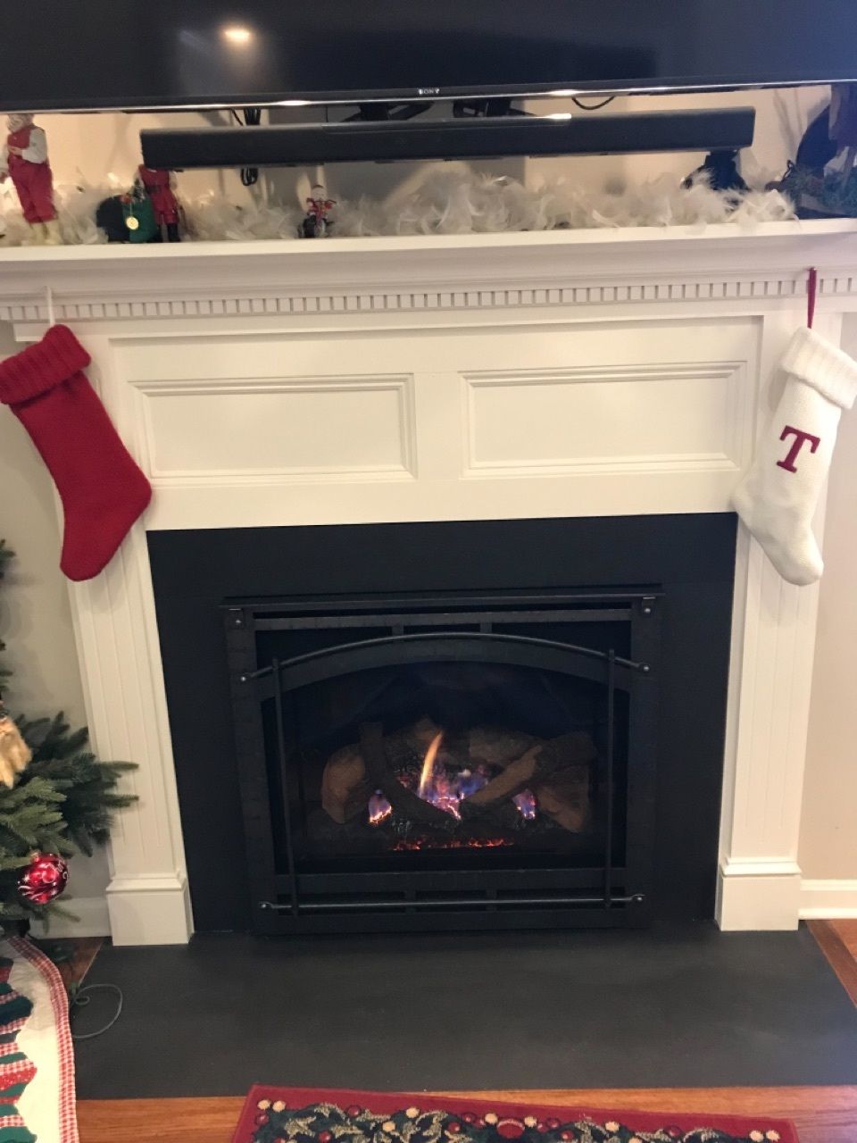 A fireplace in a living room with a christmas tree and stockings on it.