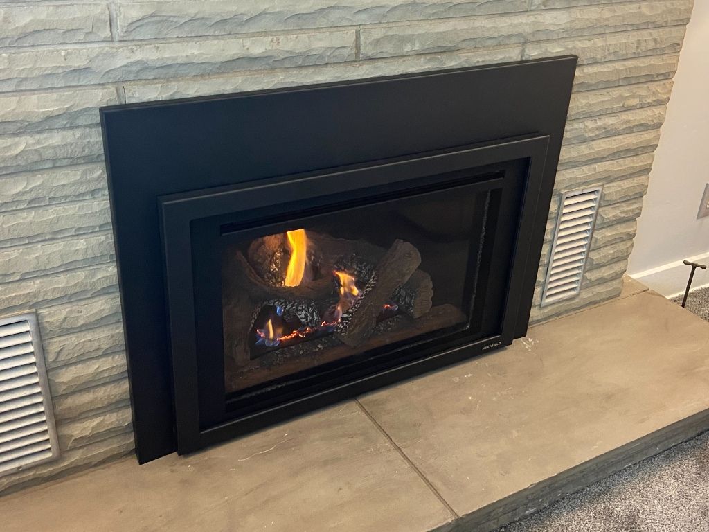 A gas fireplace is sitting in a living room next to a brick wall.