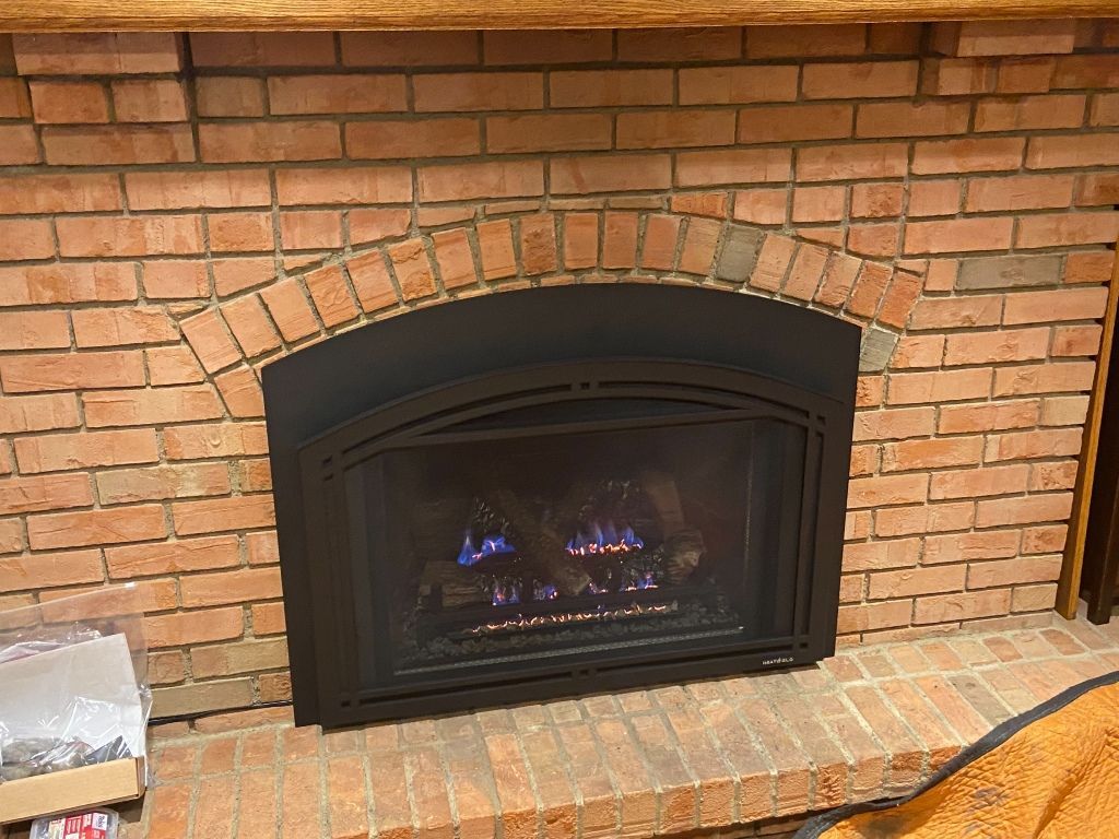 A brick fireplace with a black trim and a blue flame coming out of it.