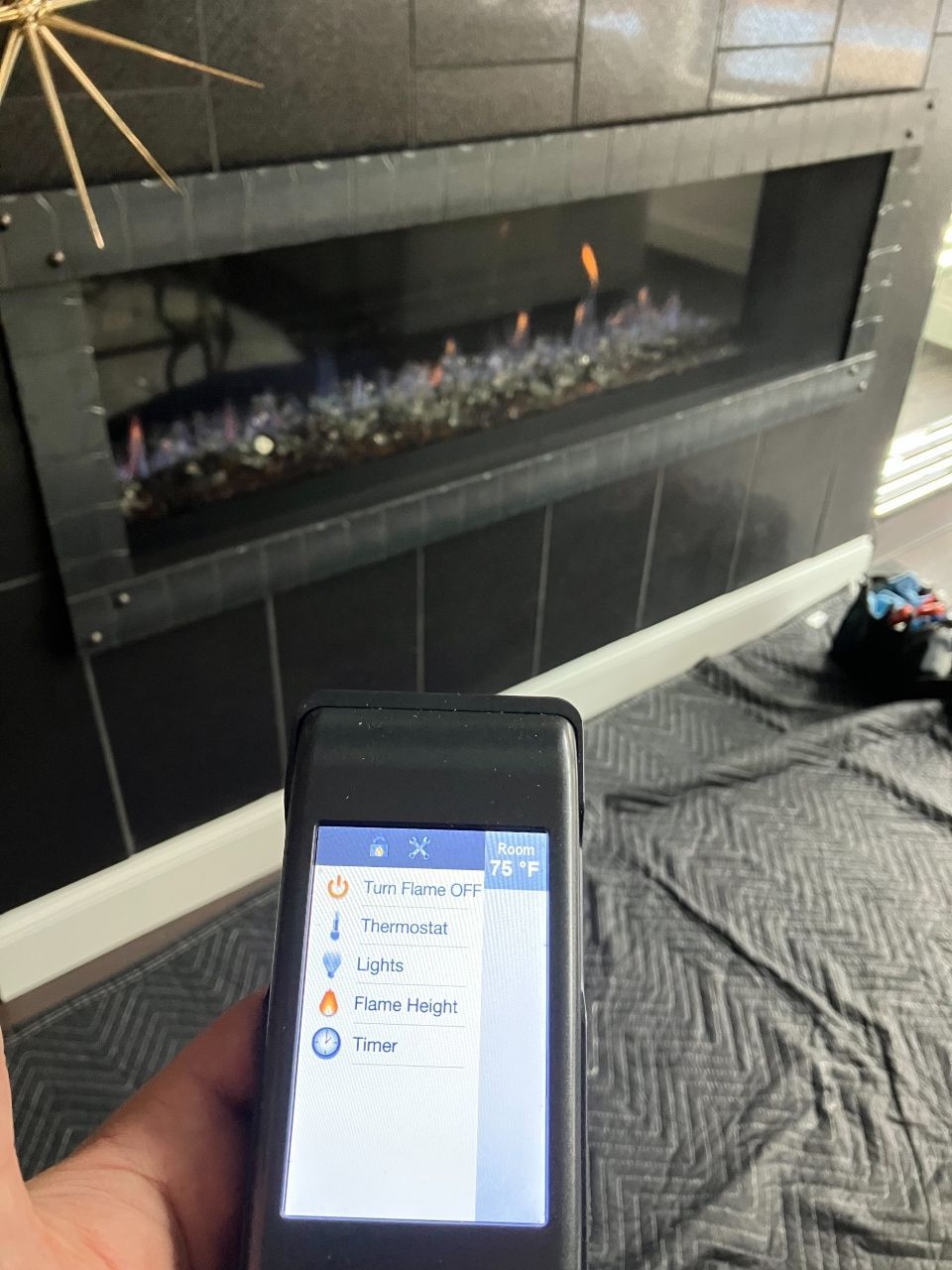 A person is holding a remote control in front of a fireplace.