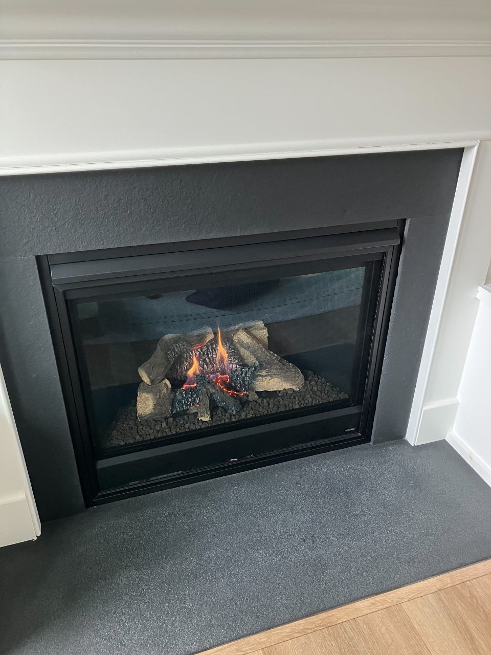 A gas fireplace is sitting in a living room next to a mantle.