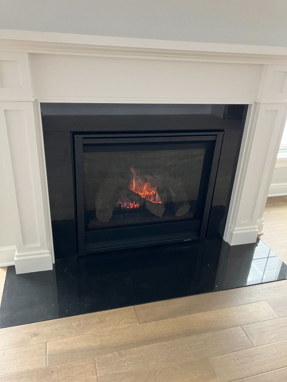 A fireplace with a black tile floor and a white mantle in a living room.