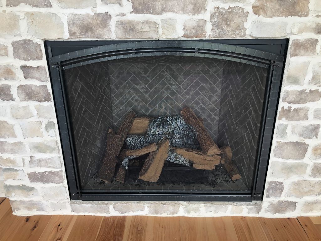 A fireplace with a screen and a lot of logs in it.