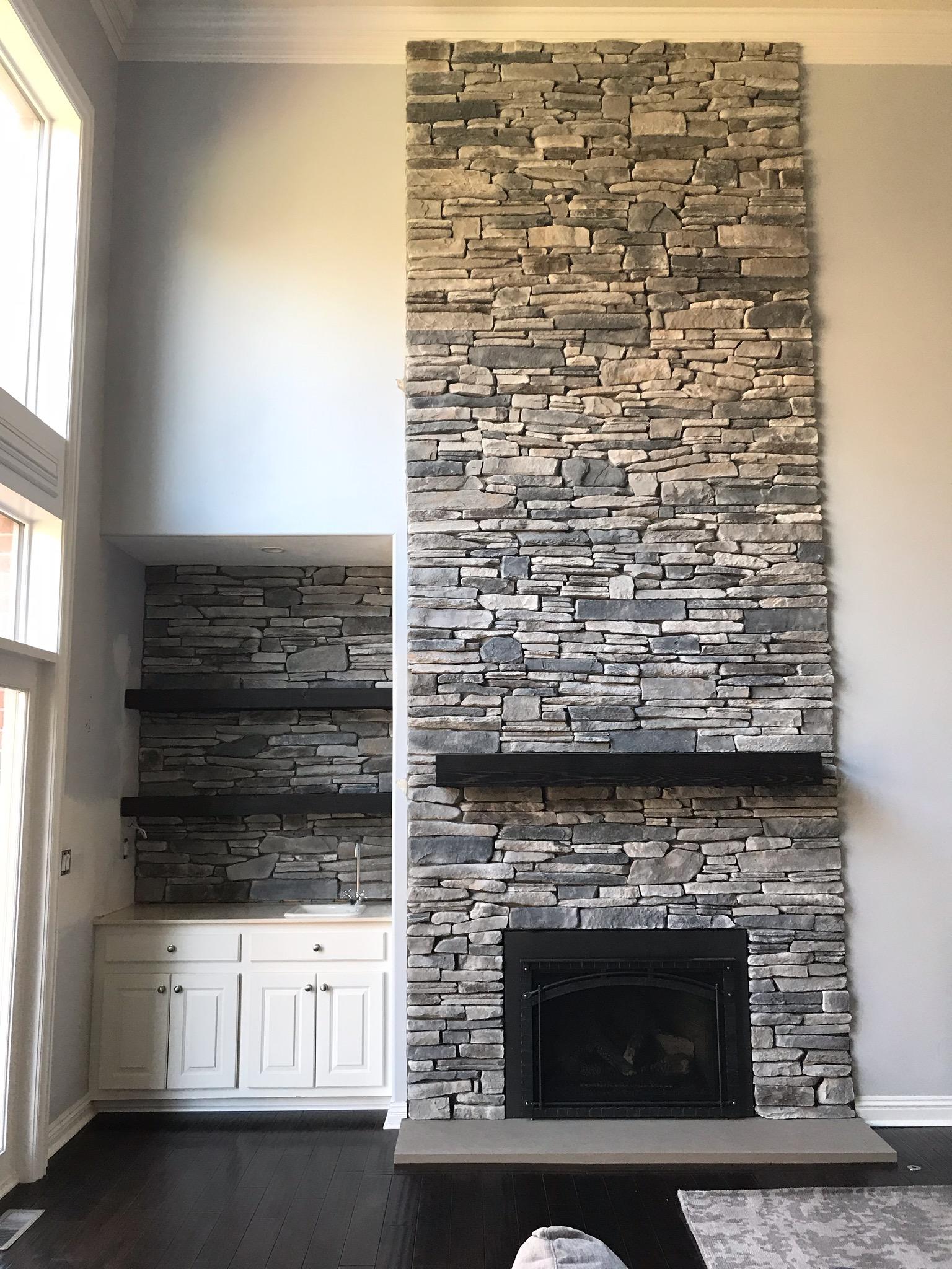 A living room with a large stone fireplace and shelves.