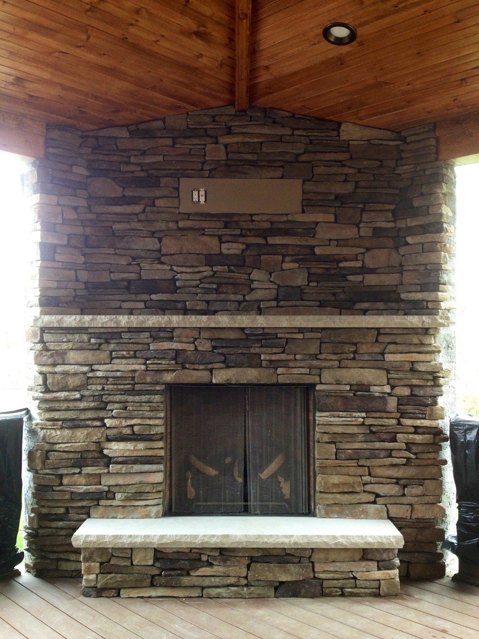 A large stone fireplace in a living room with a wooden ceiling.
