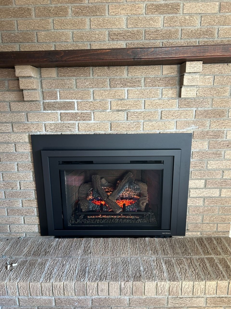 A brick fireplace with a black fireplace insert and a wooden mantle.