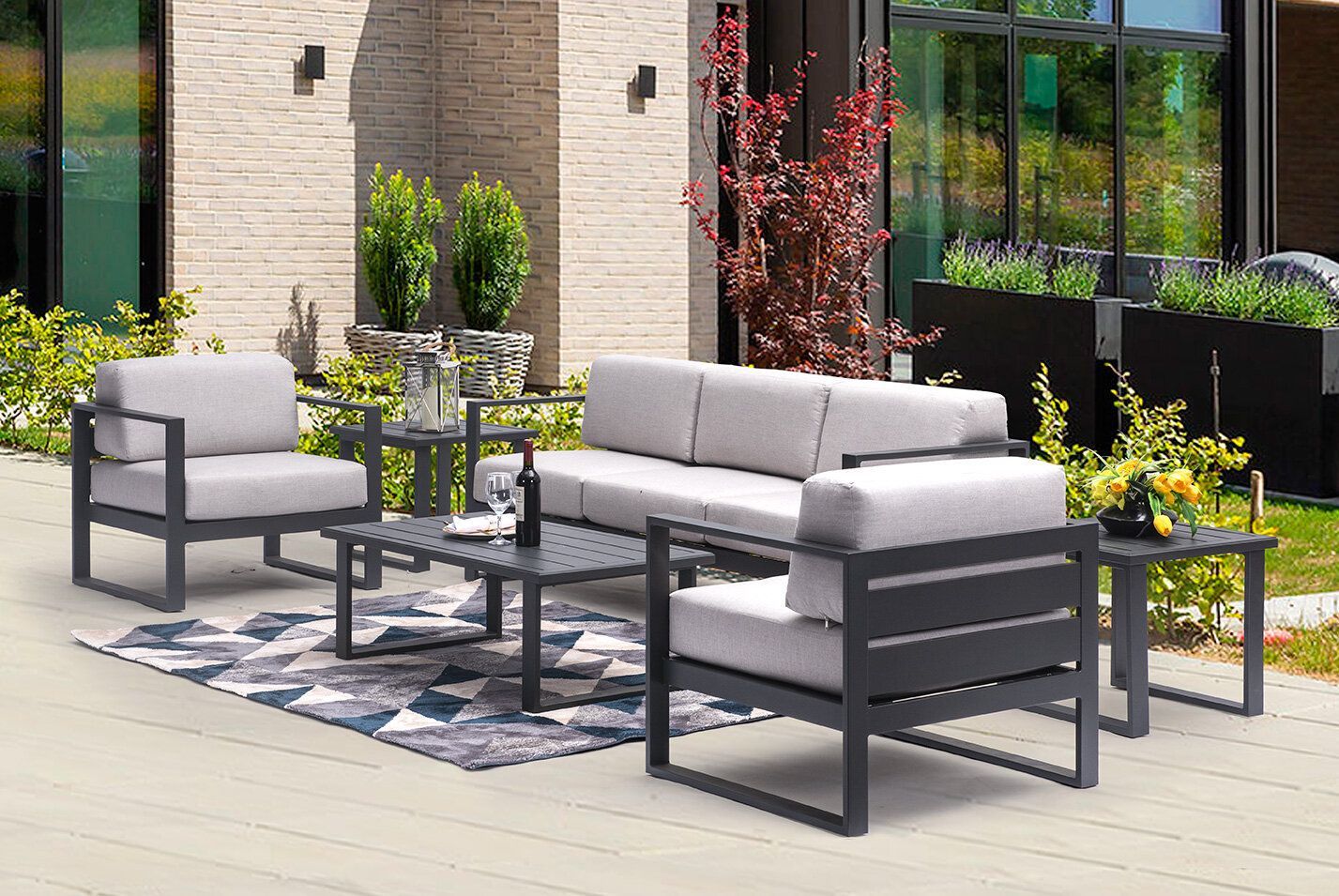 A patio with a couch , chairs , tables and a rug.