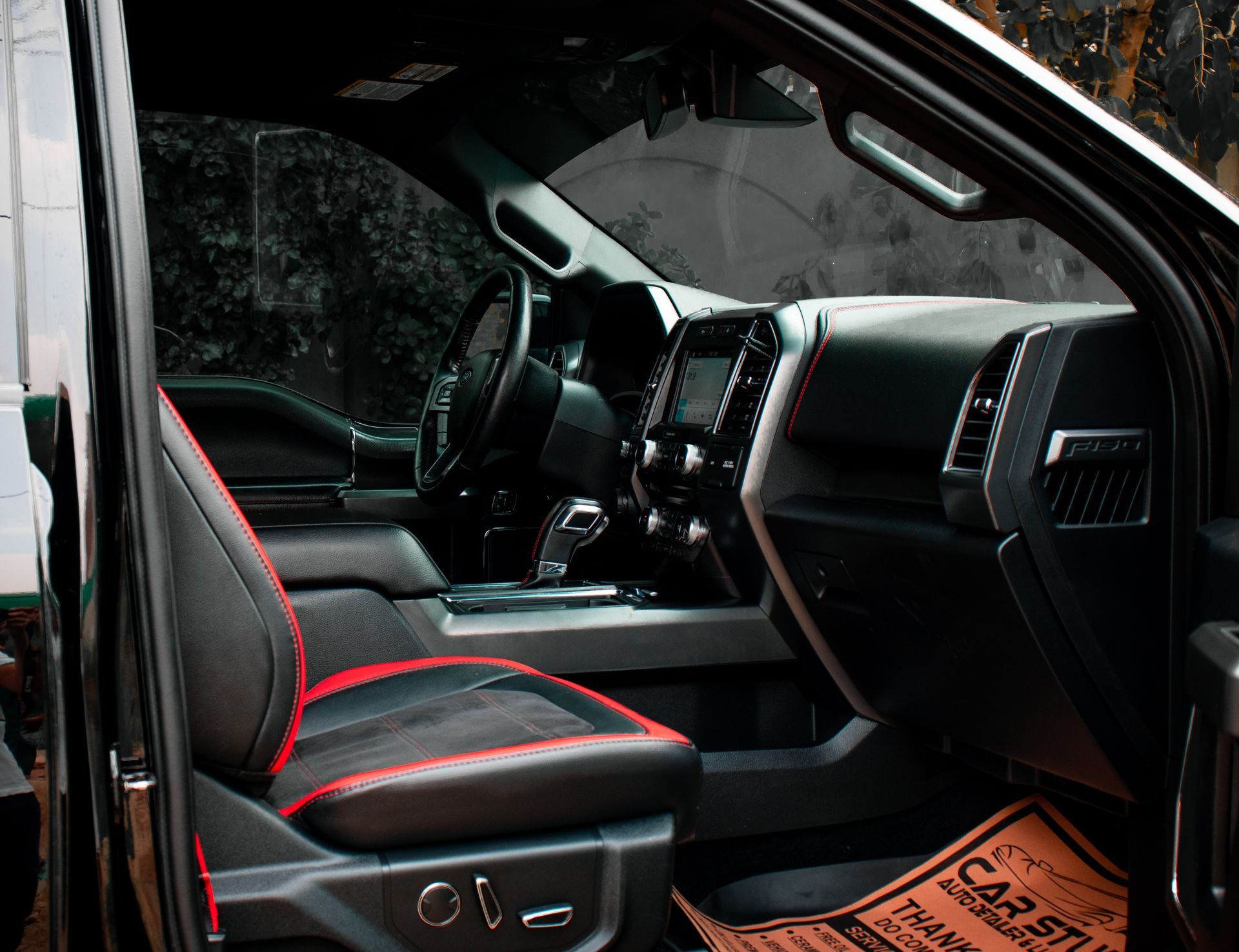 Black car interior with red-accented seats and dashboard viewed from the open door