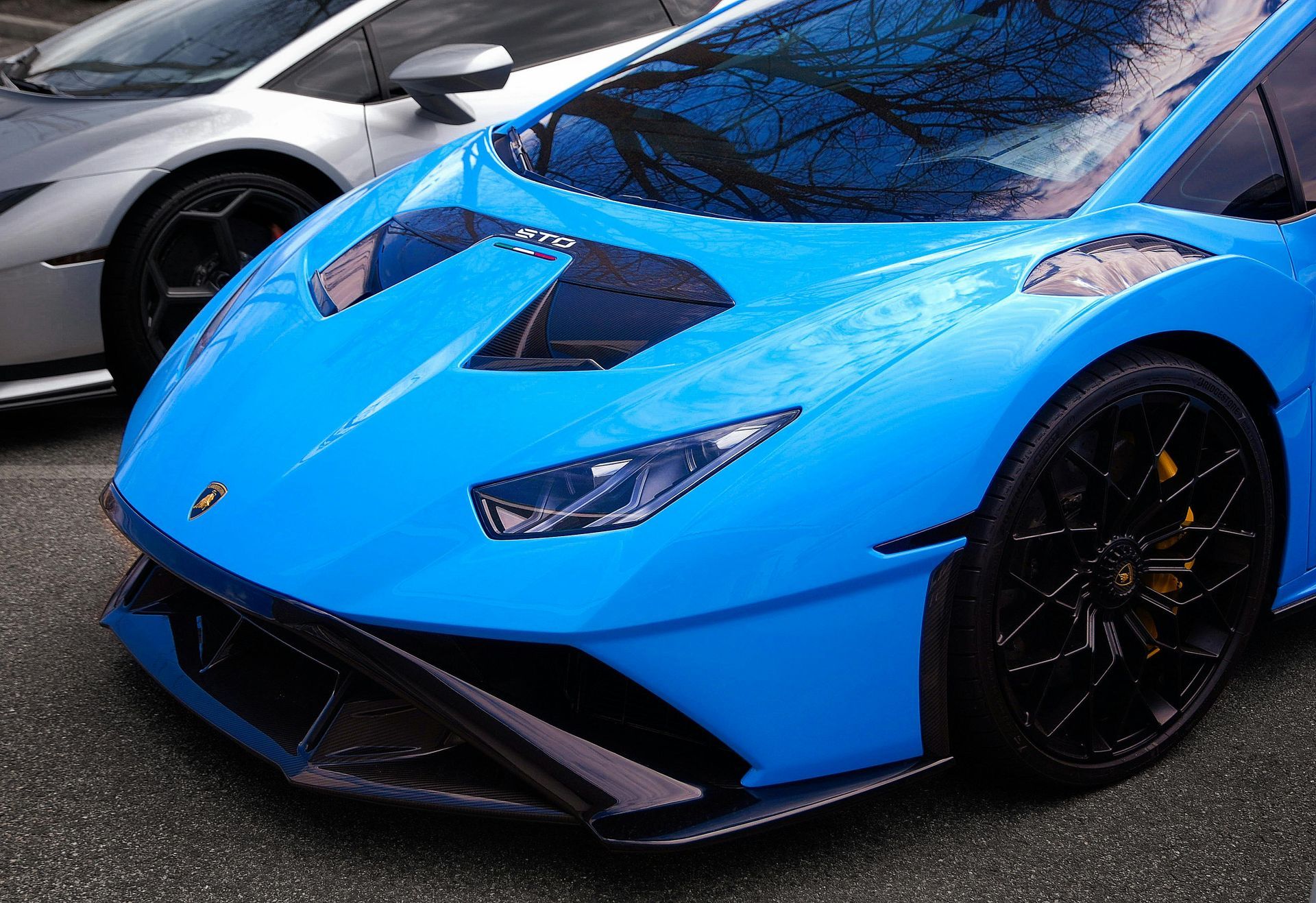 Blue Lamborghini sports car parked outdoors with a silver car beside it