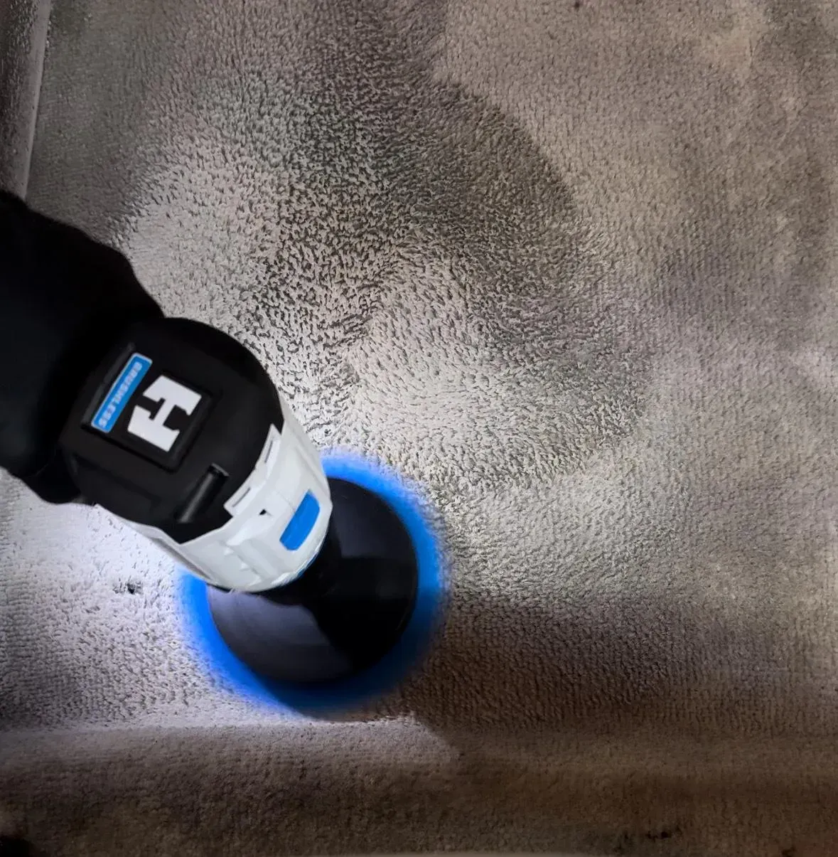 A cordless drill cuts a hole in a concrete surface, with blue light around the drill bit.