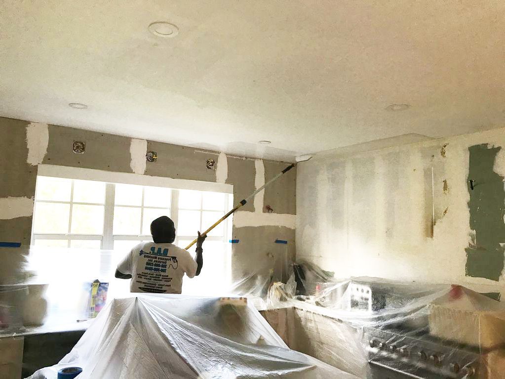 A man is painting the ceiling of a kitchen with a paint roller.