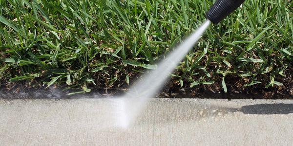 A person is using a high pressure washer to clean a sidewalk.