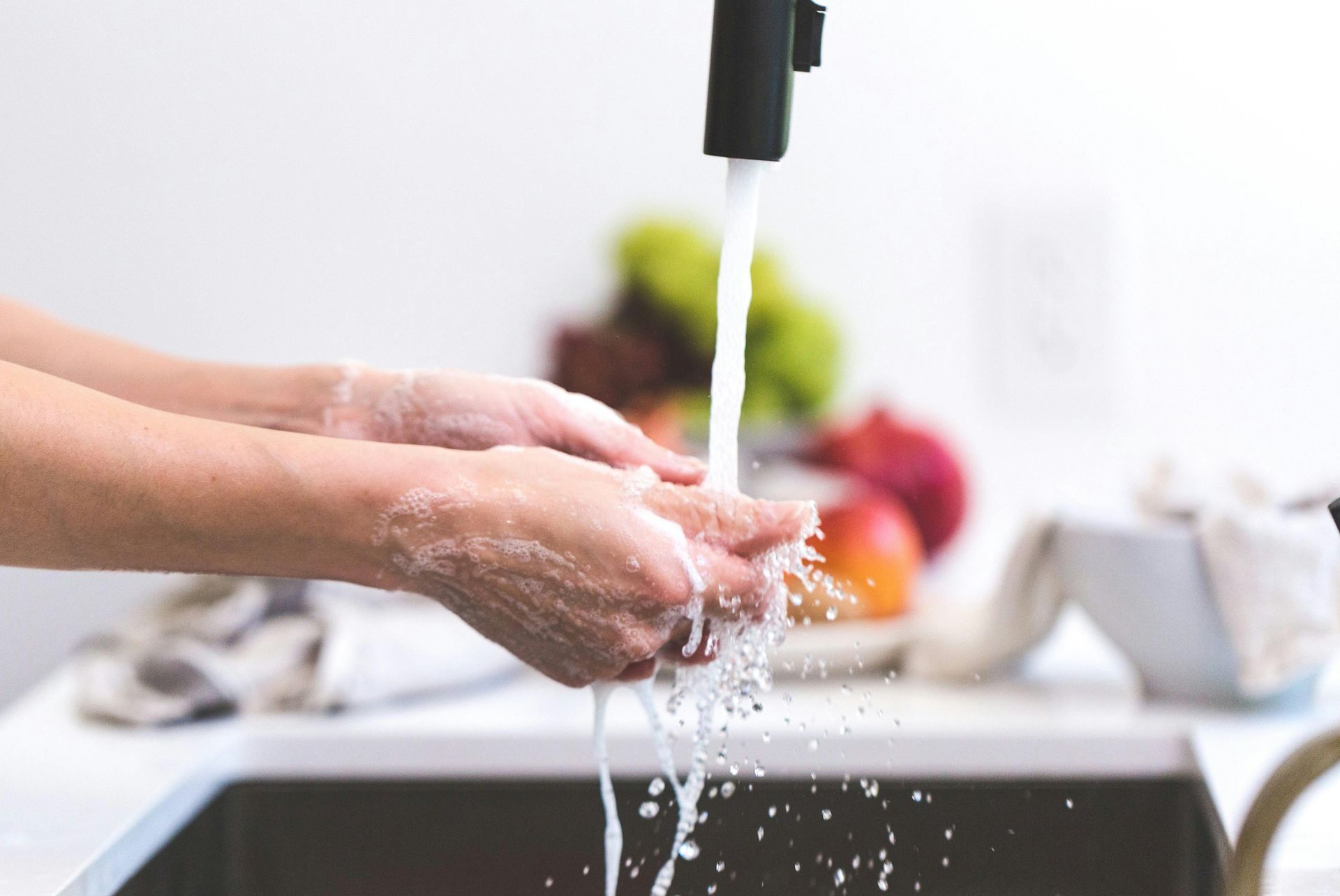 Hands washing under running water in a white kitchen sink.