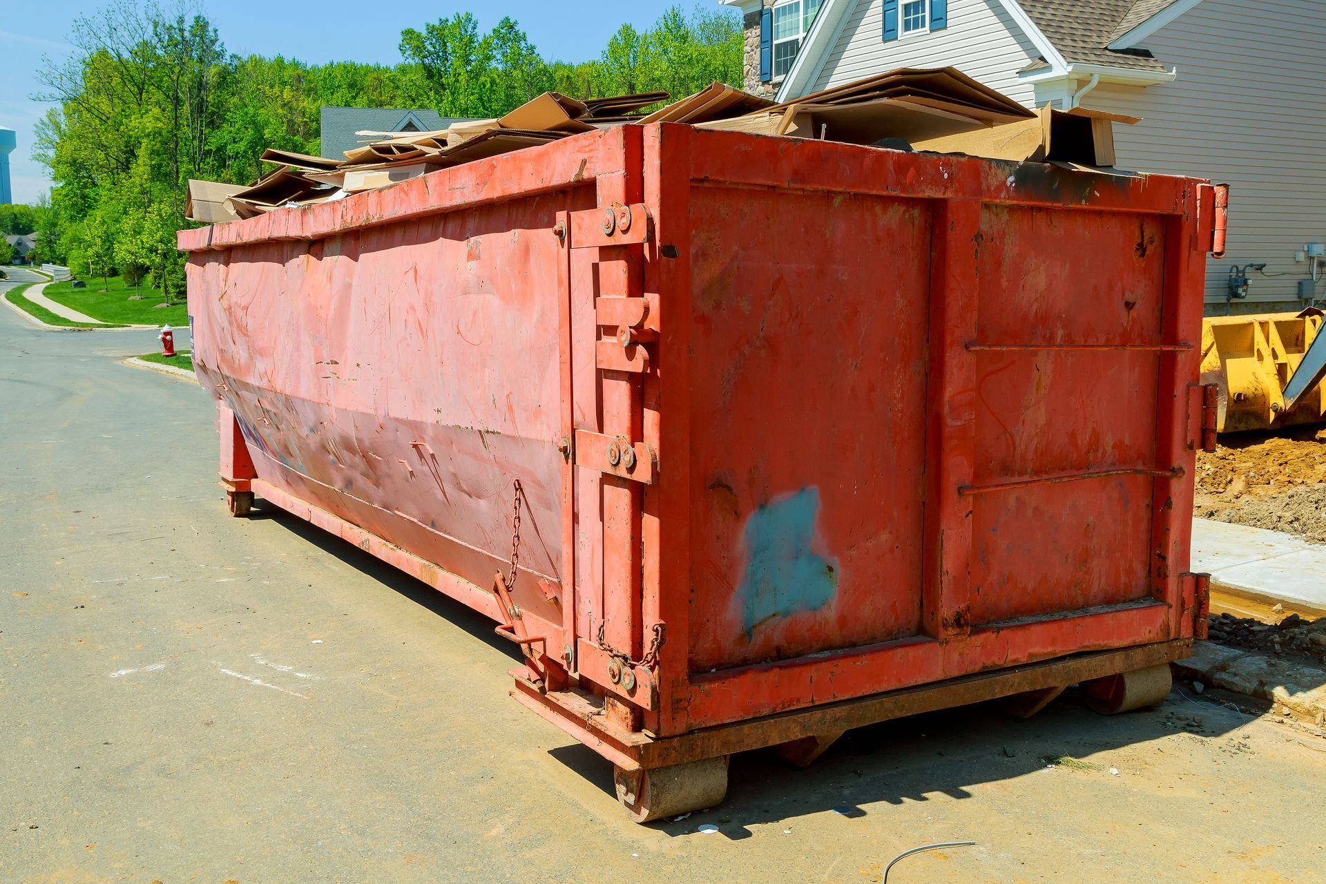 Red dumpster filled with debris on a street, likely at a construction site.