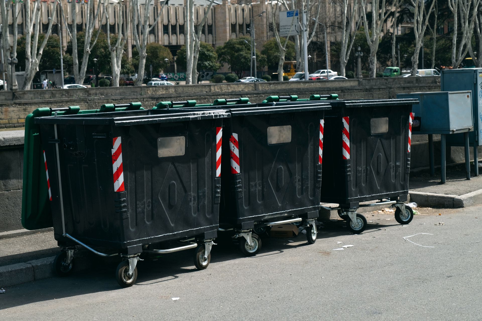 Row of black commercial dumpster rental containers on city sidewalk for business waste disposal.