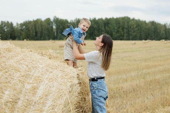 Mother lifting a child in a field of hay bales. They are smiling; the setting is a sunny day.