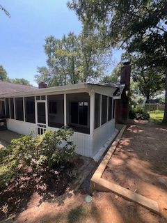 Screened-in porch attached to a white house with a brick chimney and brown dirt path.