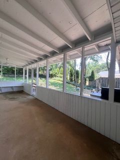 Screened porch with white walls, ceiling, and trim, overlooking a backyard with trees.
