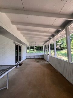 Covered porch with white brick wall, wooden beams, and a concrete floor.