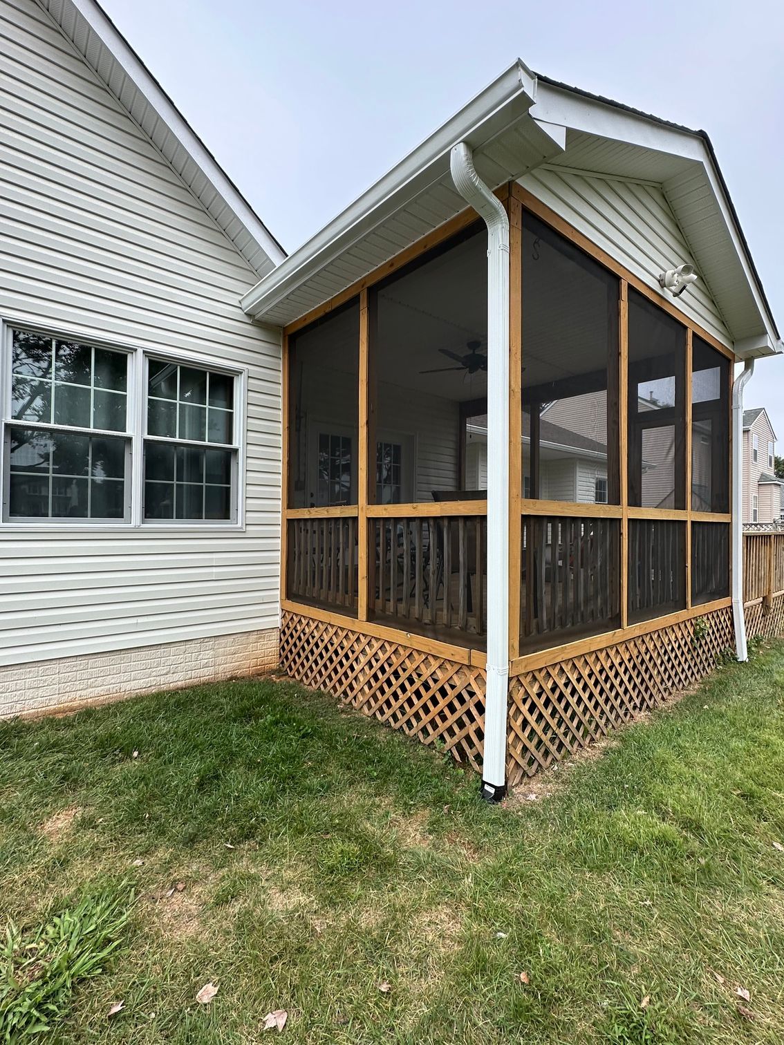 Screened-in porch attached to a white house with lattice base, brown trim, and green grass.