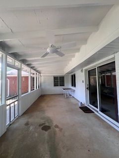 Covered porch with white ceiling, ceiling fan, screened windows, and sliding glass doors. Concrete floor.