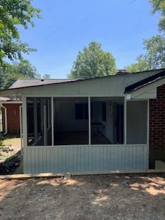 Screened-in porch attached to a brick house with a blue sky background. The porch is white.