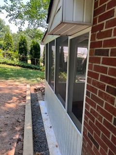 Screened porch attached to brick house, white trim, with yard and trees in the background.
