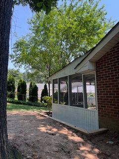 Screened-in porch attached to a brick house, next to a tree and yard.