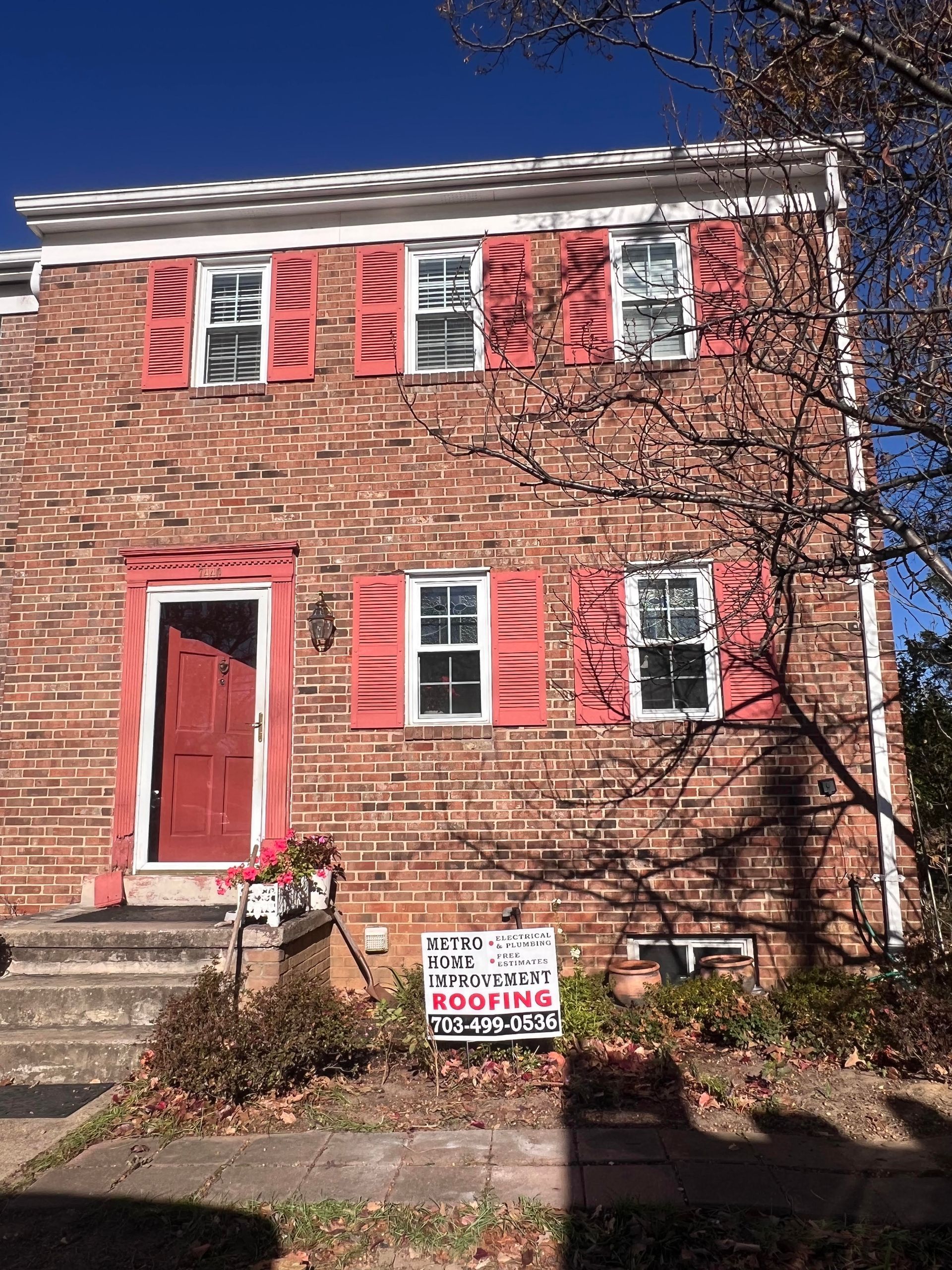 Brick house with red shutters and door. Sign in the yard.