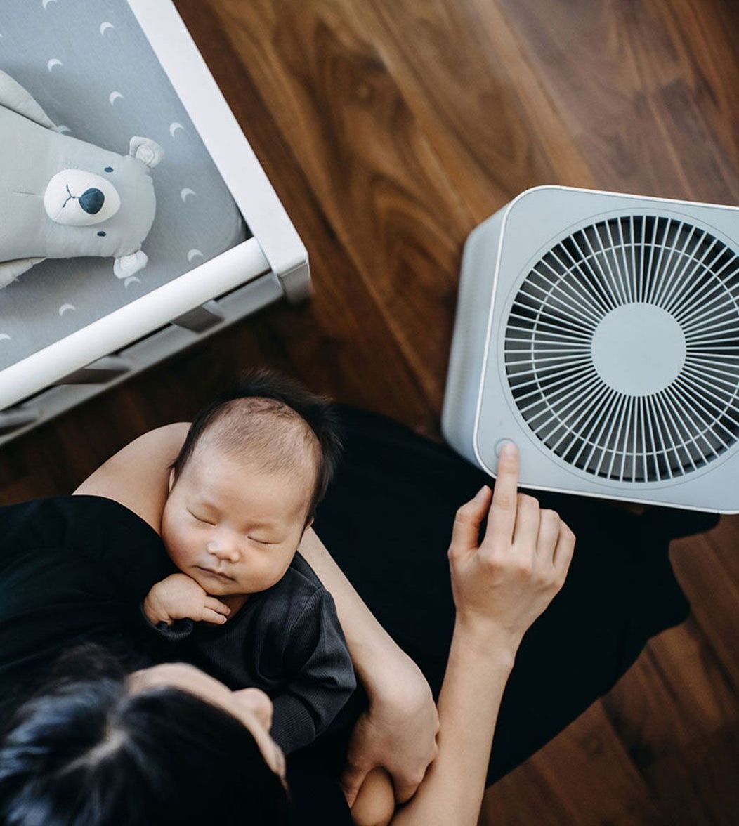 A woman is holding a baby next to a fan.