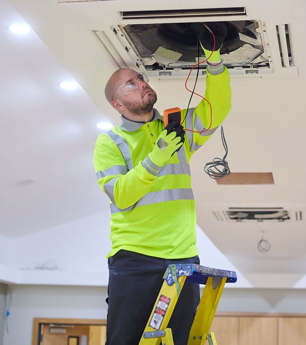 A man is standing on a ladder working on an air conditioner.