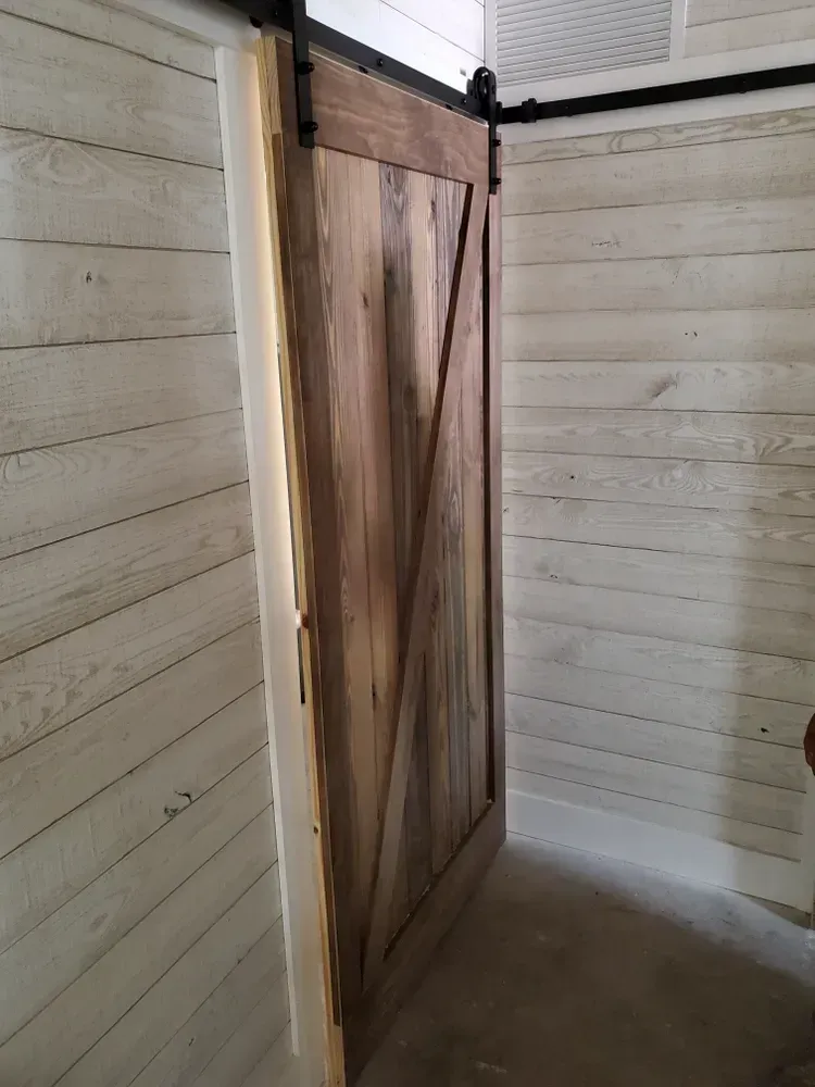 A wooden sliding barn door is hanging on a white wall in a room.