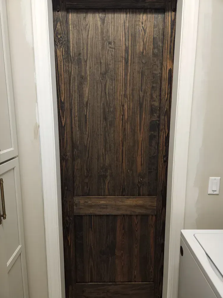 A wooden door is in a laundry room next to a washer and dryer.