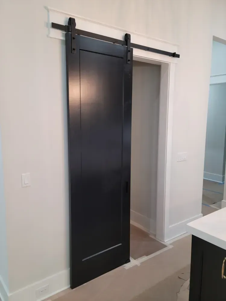 A black sliding barn door is hanging on a white wall in a kitchen.