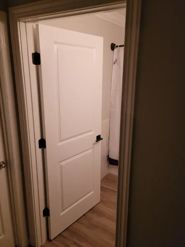 A white door is open to a bathroom with a shower curtain hanging on the wall.
