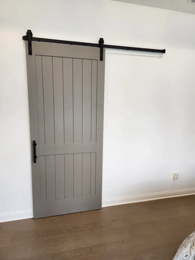A gray sliding barn door is hanging on a white wall in a bedroom.