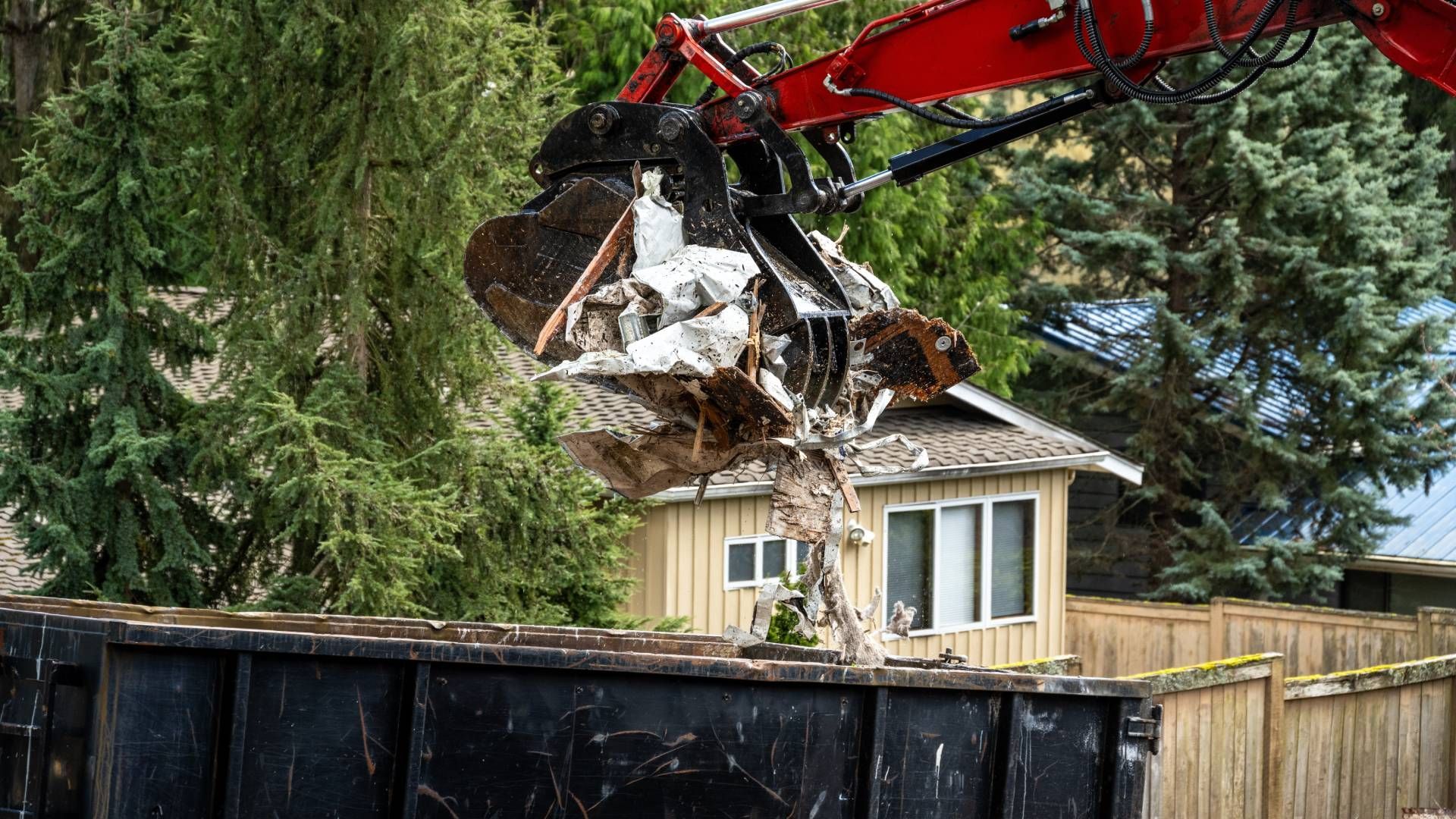 A crane is lifting a piece of metal into a dumpster.