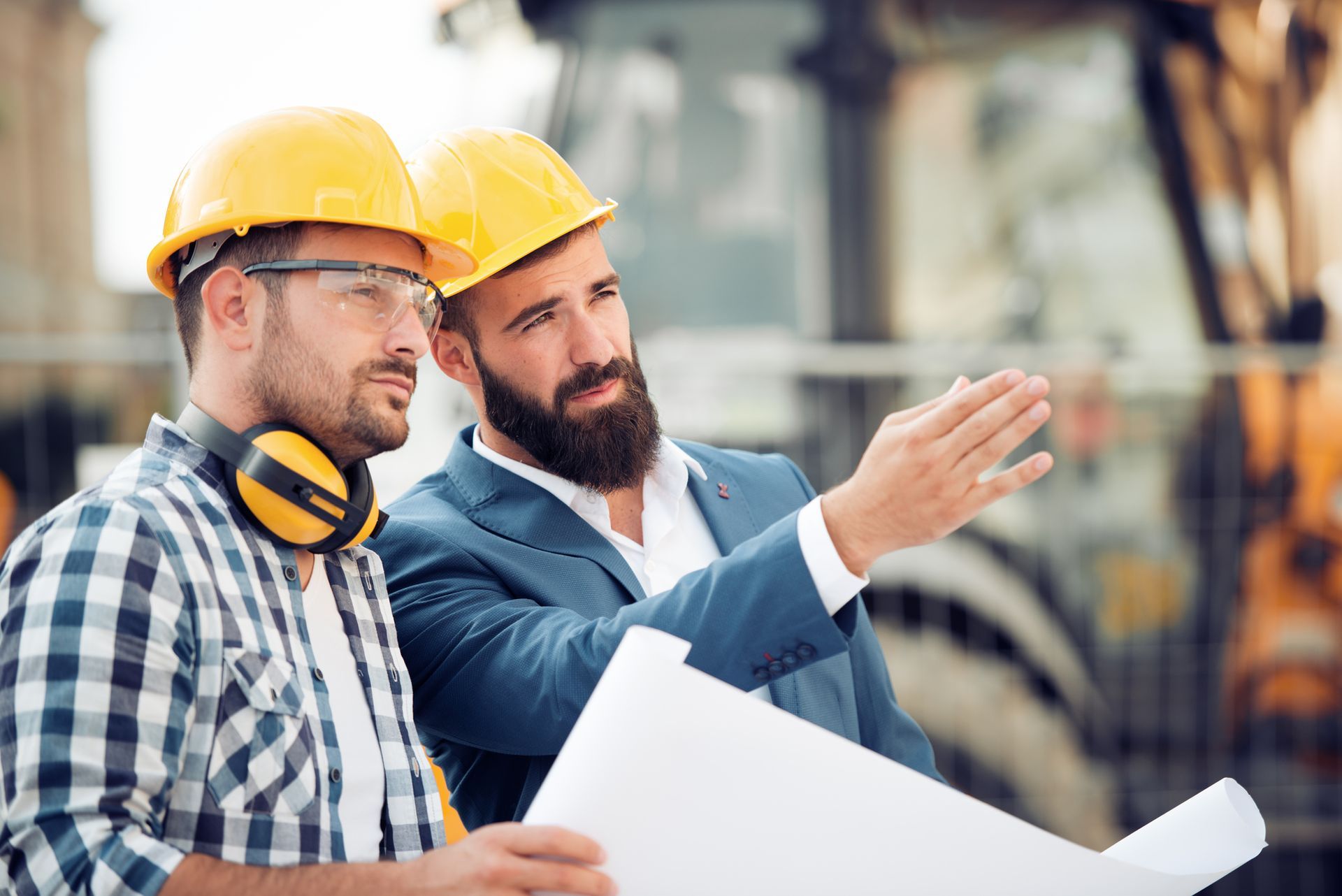 Two construction workers are looking at a blueprint on a construction site.