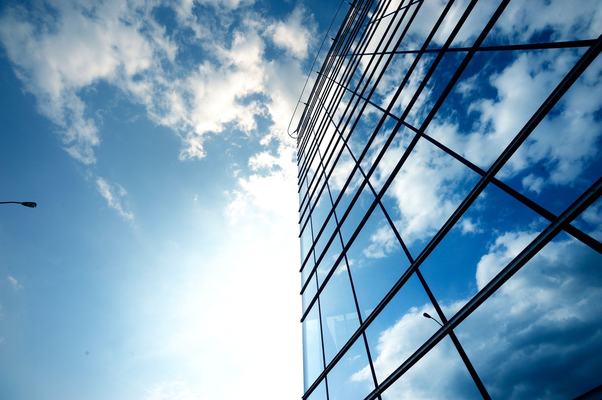 Looking up at a tall building with a blue sky and clouds reflected in the windows