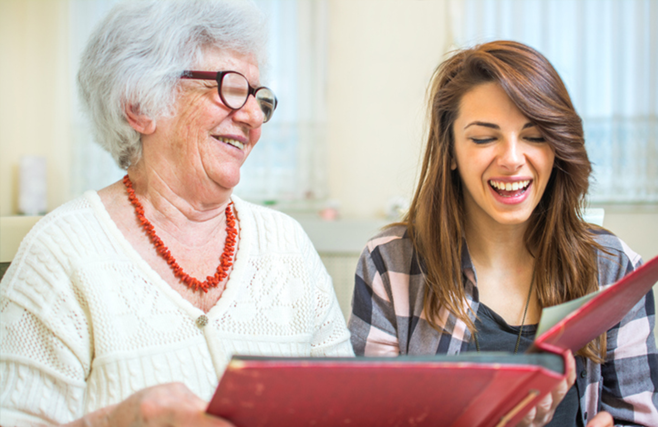 an elderly woman and a young woman are looking at a photo album .