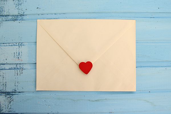 an envelope with a red heart sticking out of it on a blue wooden table .