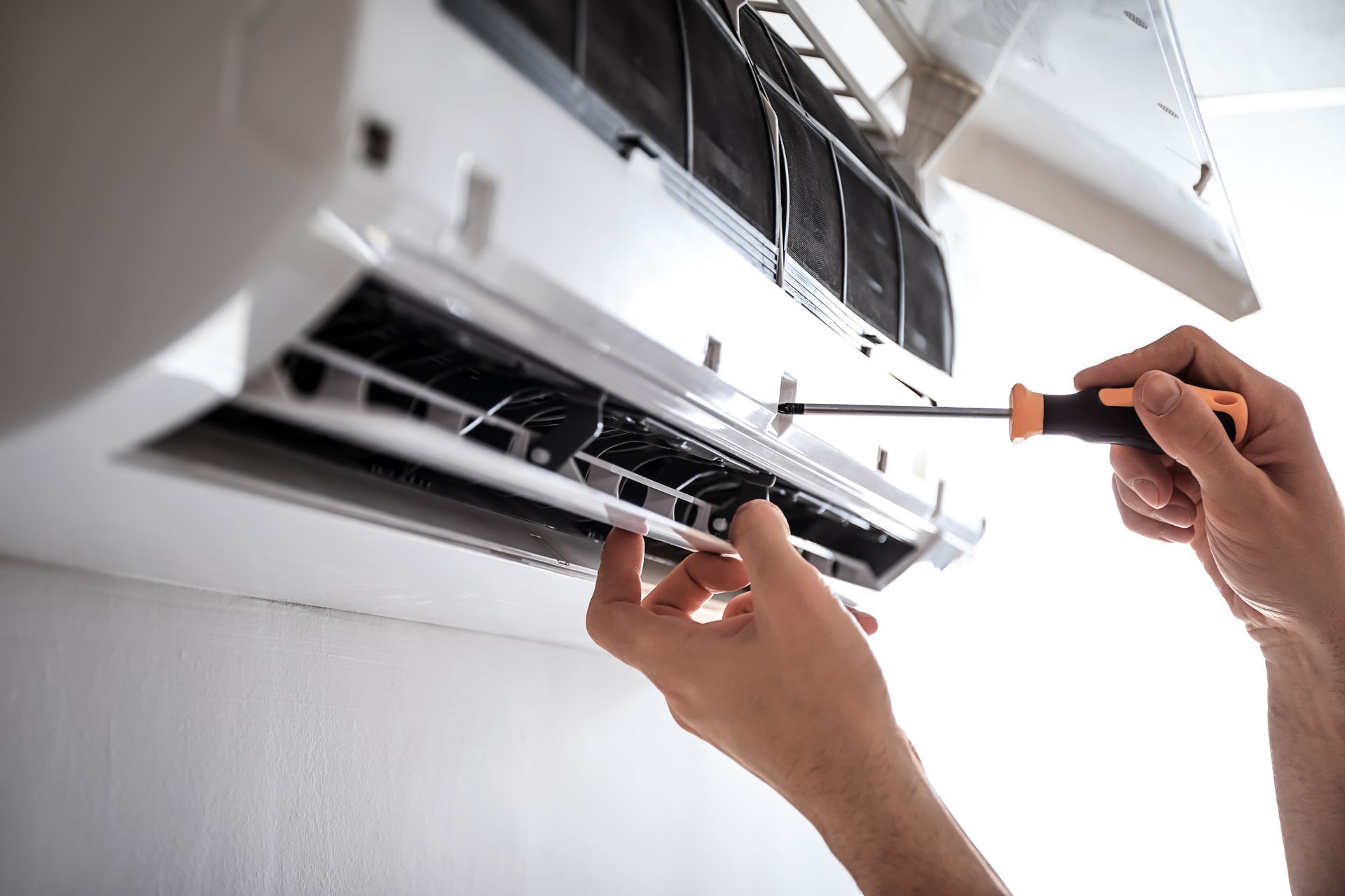 The technician installs the wall-mounted air conditioner with a screwdriver.