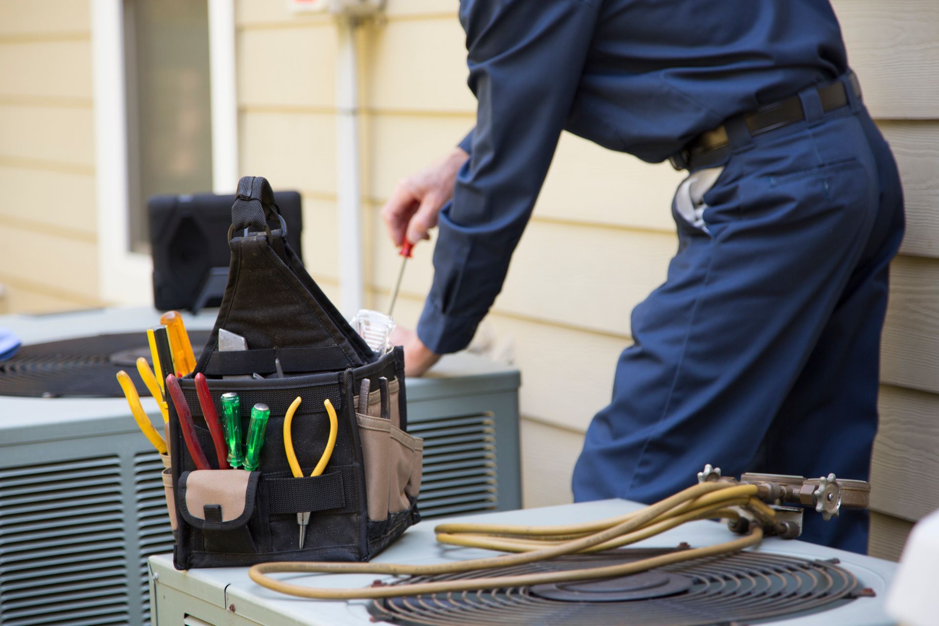 Close-up of a heating contractor wearing a blue uniform, servicing outside AC units and generator. - Medford, OR - Southern Oregon Heating & Air Conditioning, Inc.