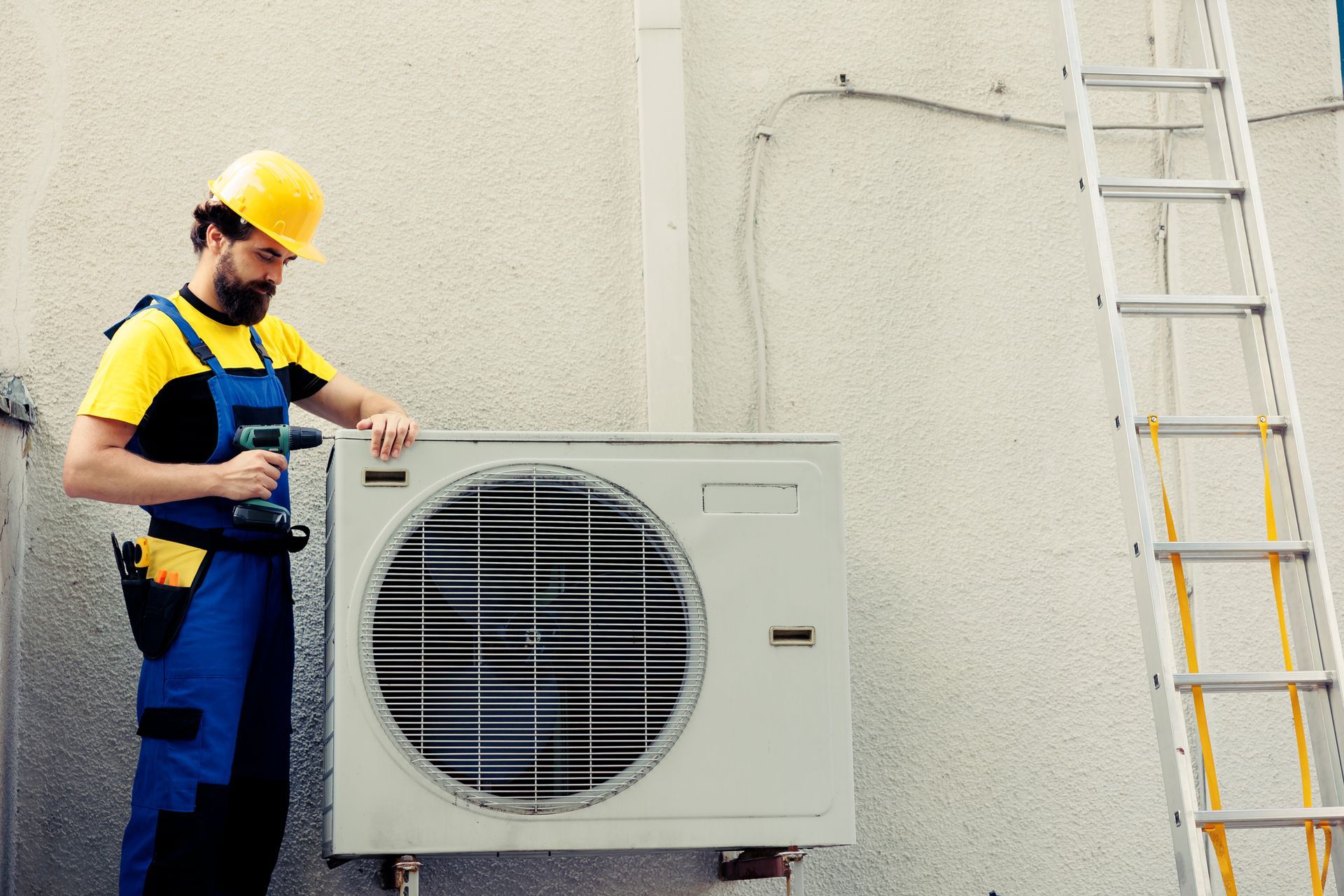 Heating contractor servicing outdoor HVAC unit with drill and safety gear beside extension ladder.