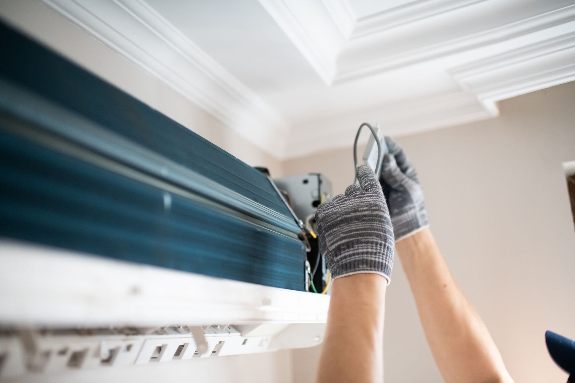 Person wearing gloves installing an air conditioning unit on the ceiling Person wearing gloves installing an air conditioning unit on the ceiling