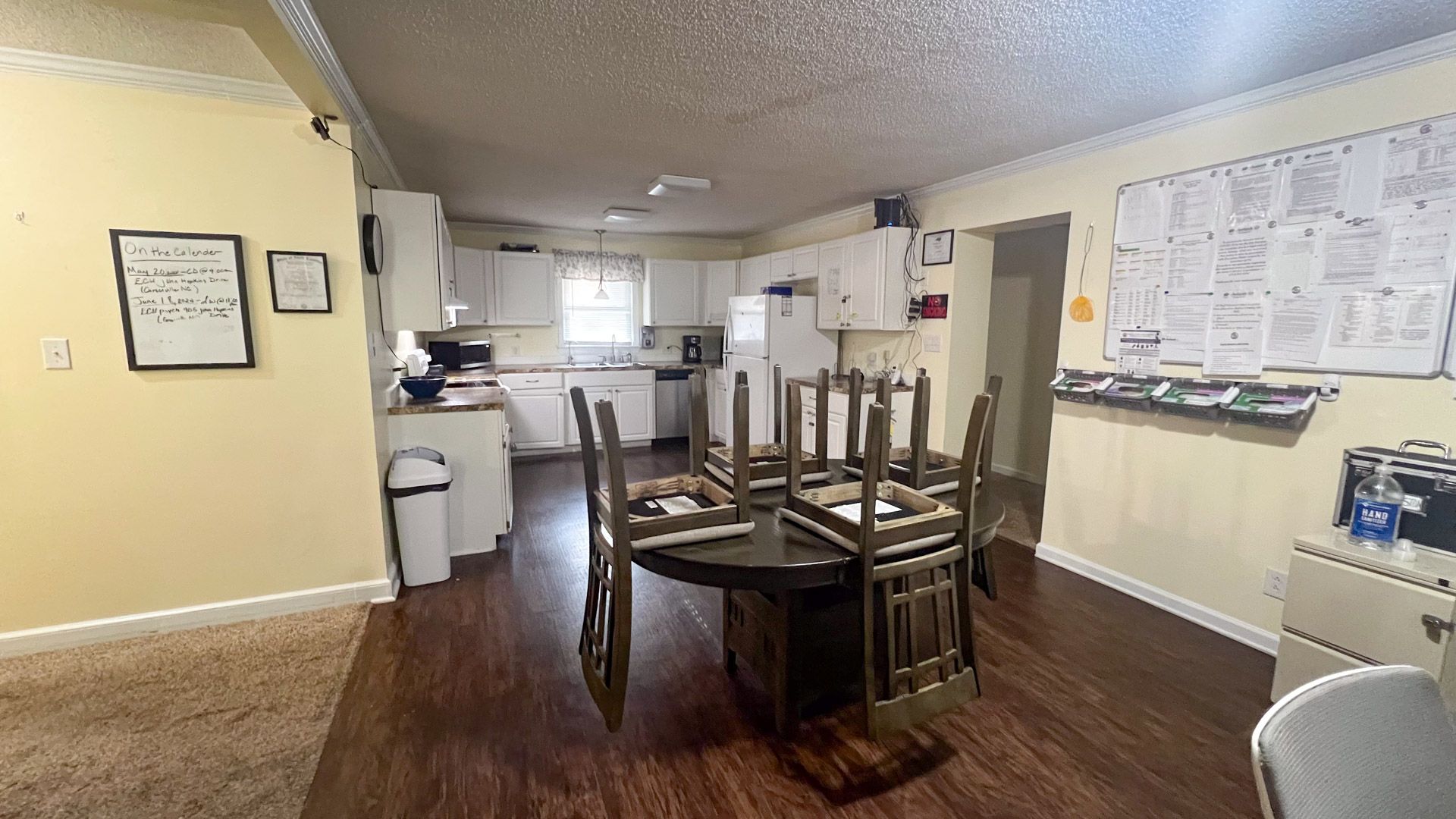 A dining room with a table and chairs in it and a kitchen in the background.
