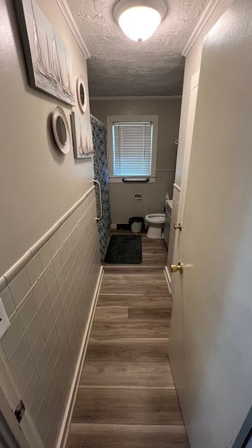 Narrow bathroom with a toilet, shower, and nautical-themed decor; neutral colors.