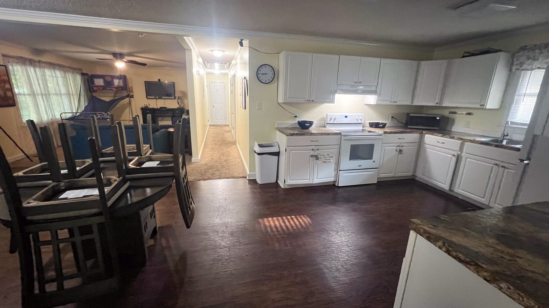 A kitchen with a stove , sink , chairs and a clock on the wall.